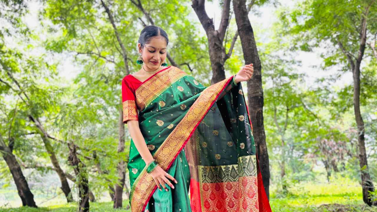 Woman in a beautiful traditional saree posing gracefully in a lush, green outdoor setting.