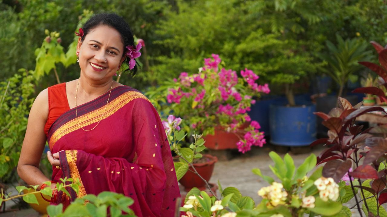 Mastering the First Impression: Your intriguing post title goes here South Asian woman in a red saree stands in a vibrant garden, smiling with joy.